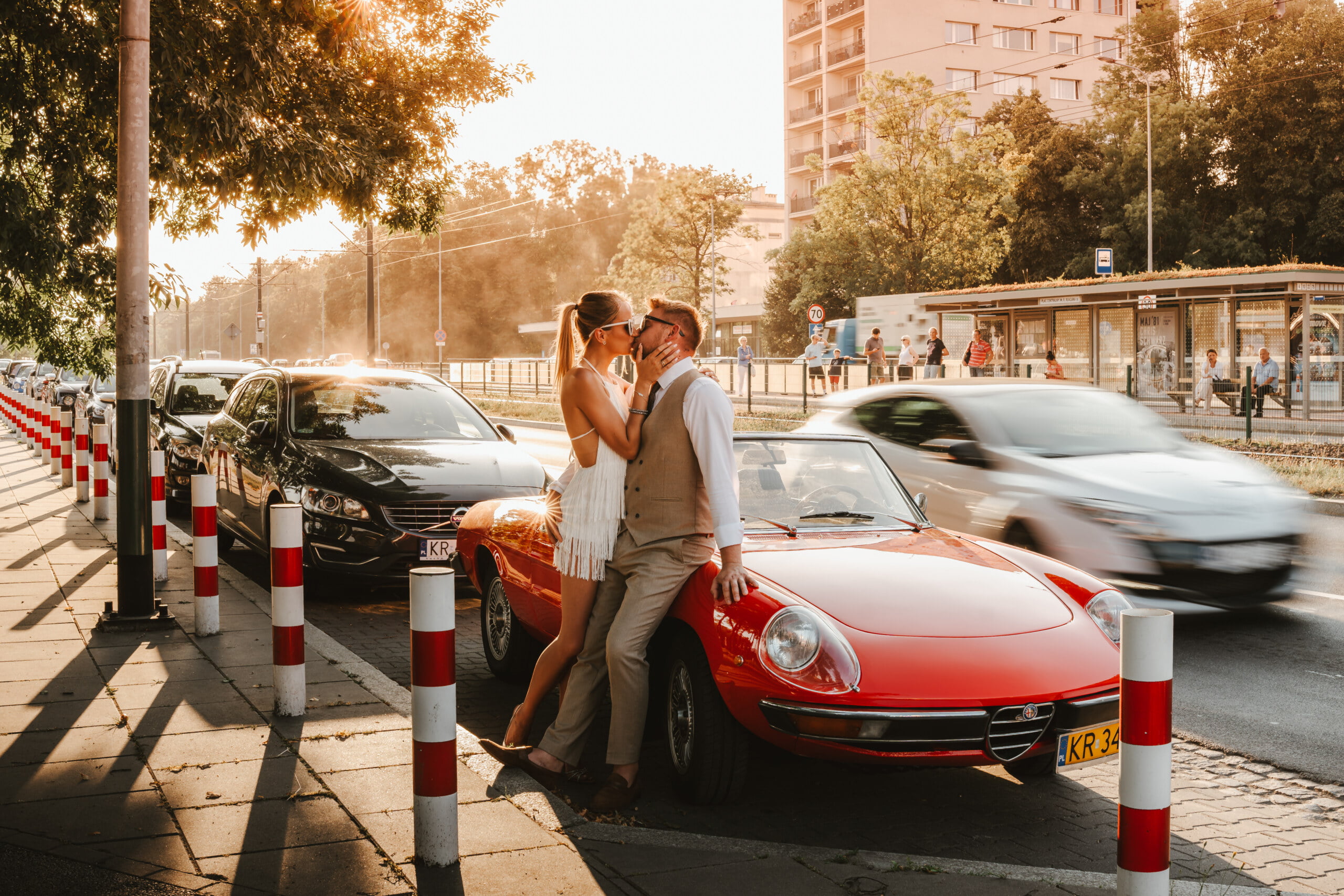 a man and woman kissing on a street corner next to a red car